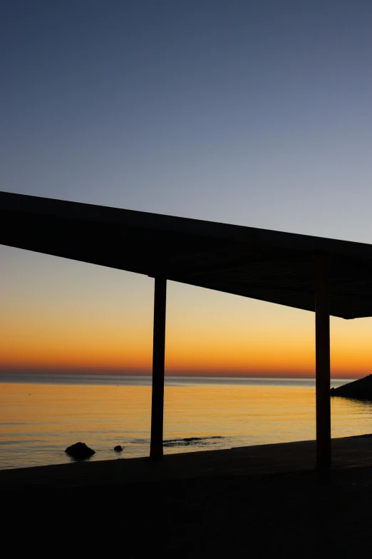 an empty beach sitting under a wooden structure next to the ocean