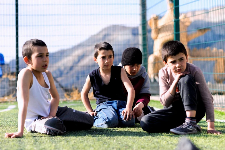 four children sit in a circle on the grass near a fence