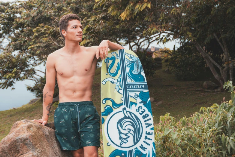 man holding up a surfboard by some bushes