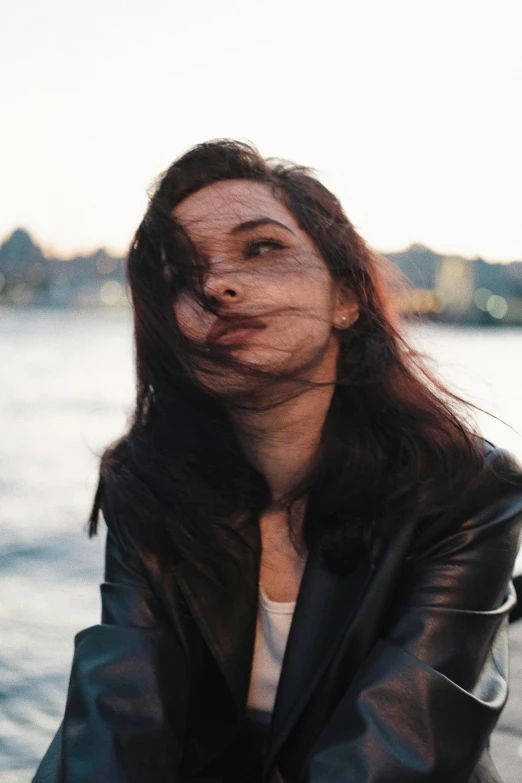 a woman in black jacket blowing nose near water