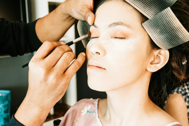 a lady being done her makeup while the hairdresser is doing it