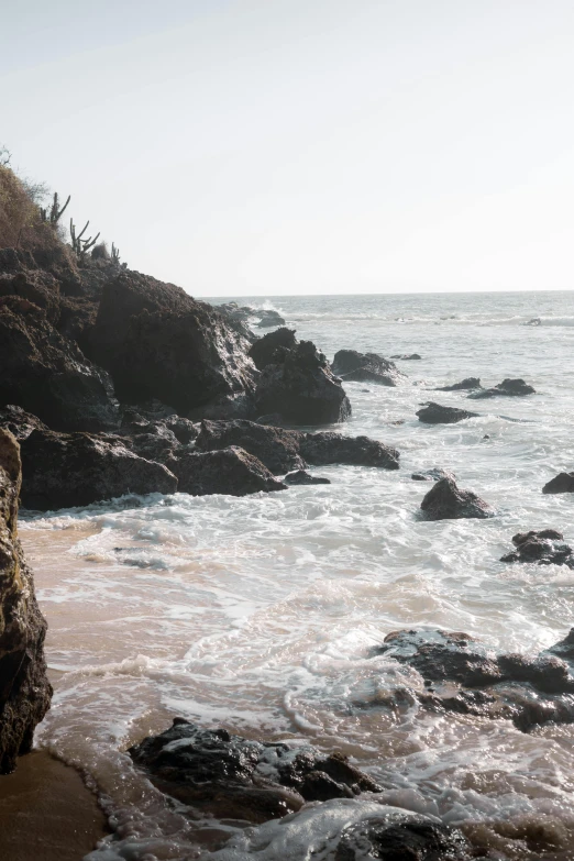 a surfer sits on the edge of the water near rocks