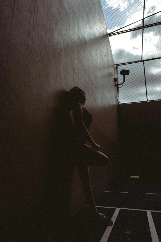 a woman standing in the corner of a building, with a sky light coming through her