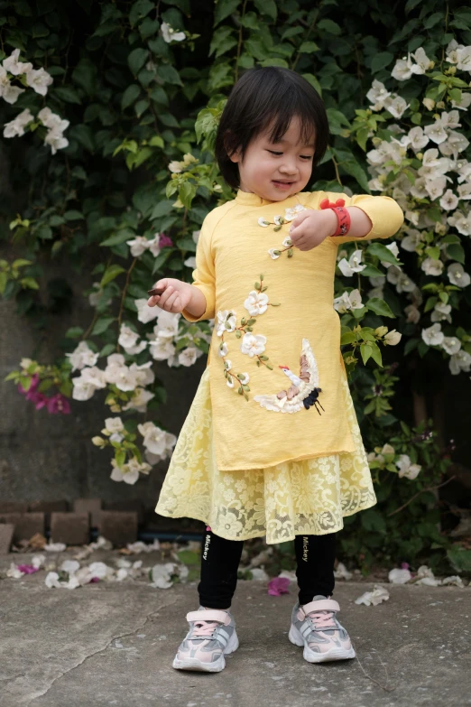 a  in a yellow dress standing next to some flowers