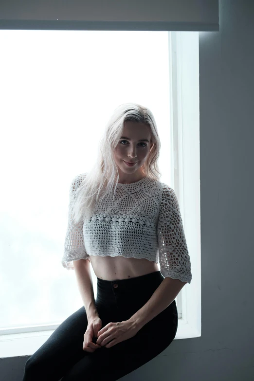 a beautiful young blonde woman sitting on a window sill