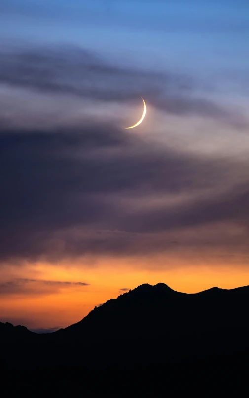 a moon in the sky as the sun sets behind mountains