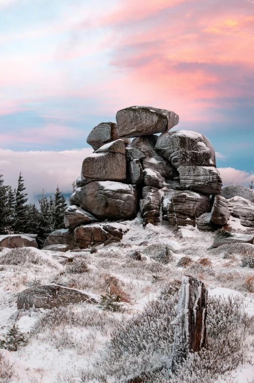 some rocks covered in snow with trees and pink clouds