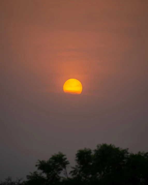 the sun sets in the sky above a tree line