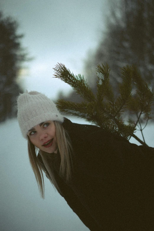 a woman standing outside in the snow with her hand under the tree