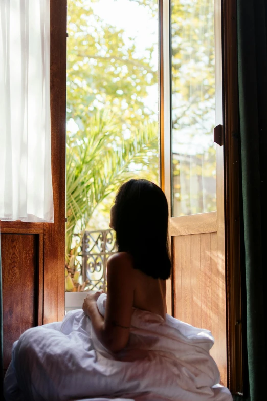 a woman sitting in bed looking out the window