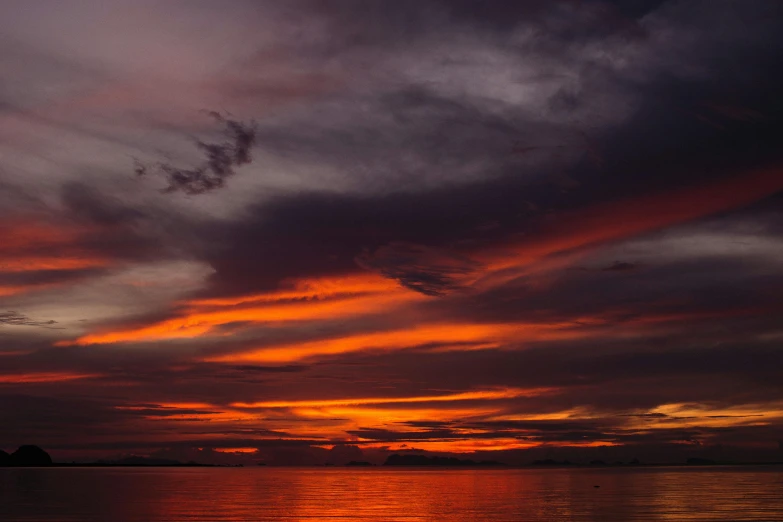 the sun sets behind a cloud filled sky over the water