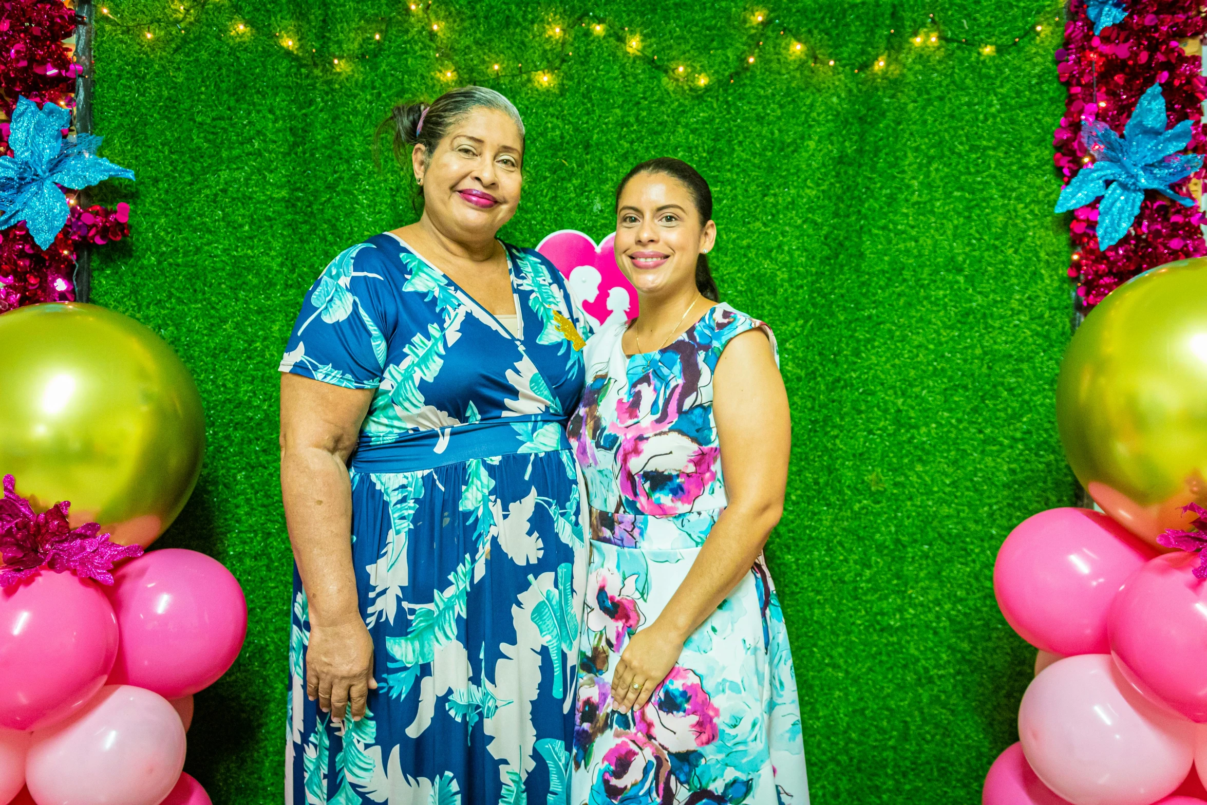 a woman and  standing in front of a green backdrop with balloons and flamingos