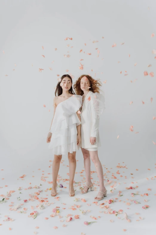 two women standing in front of pink and white petals