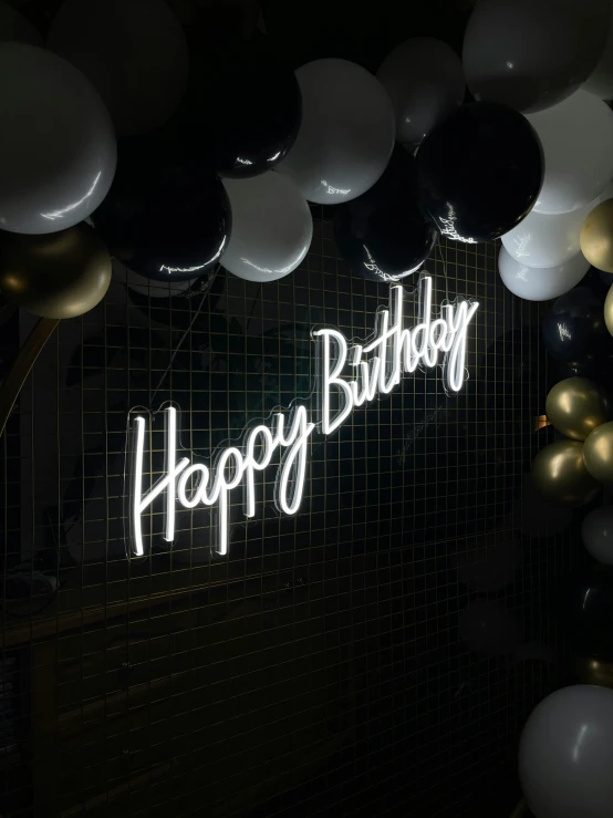 a neon sign that says happy birthday surrounded by balloons