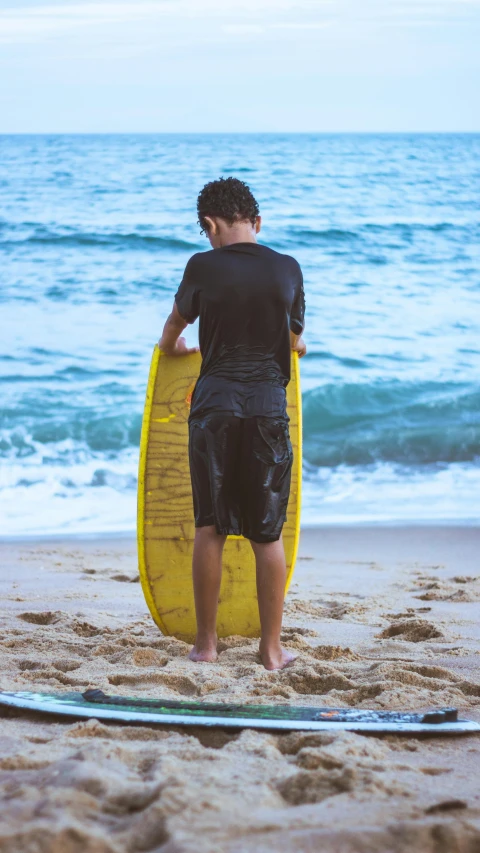 a young man standing on the beach next to his surfboard