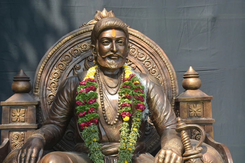 this statue depicts an indian male sitting on a throne