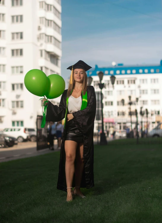 there is a female graduate holding some green balloons