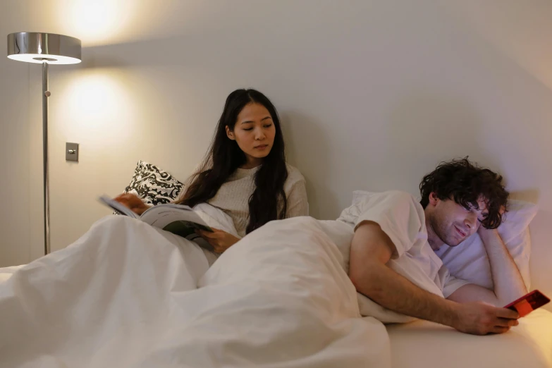 the couple is in bed reading books and looking at soing