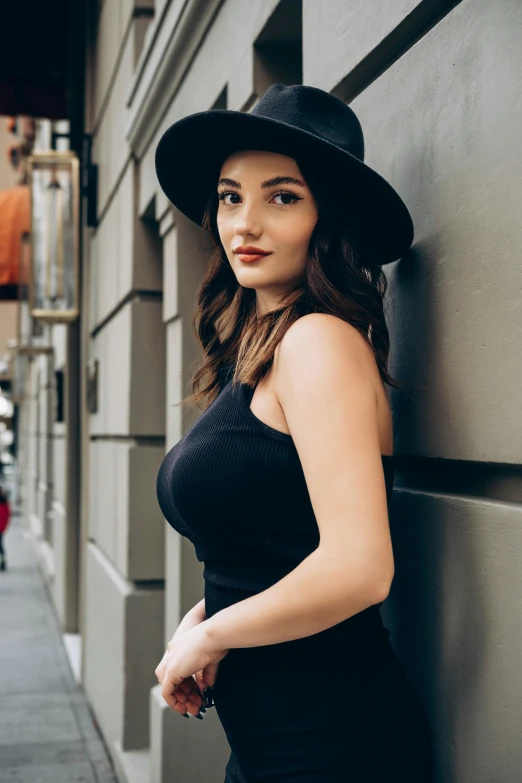 a woman standing on a sidewalk, wearing a black dress and hat