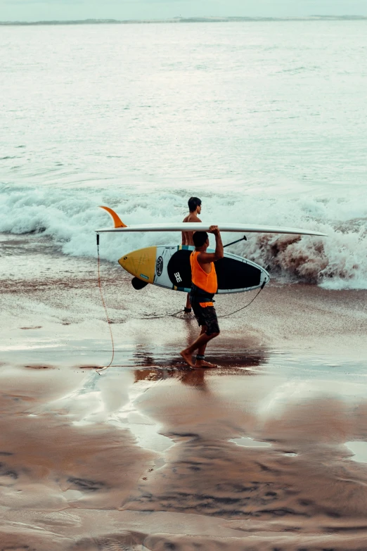 two people carry surfboards toward the ocean