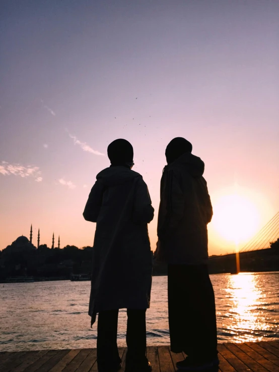 the couple is standing on the dock watching the sun set