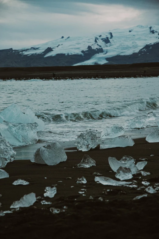 large chunks of ice are on a beach with mountains in the distance