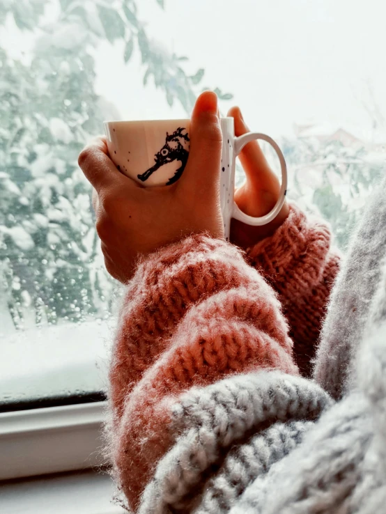 a person holding up a mug with a tree outside