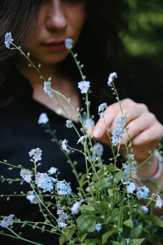 woman in black shirt holding out small blue flowers