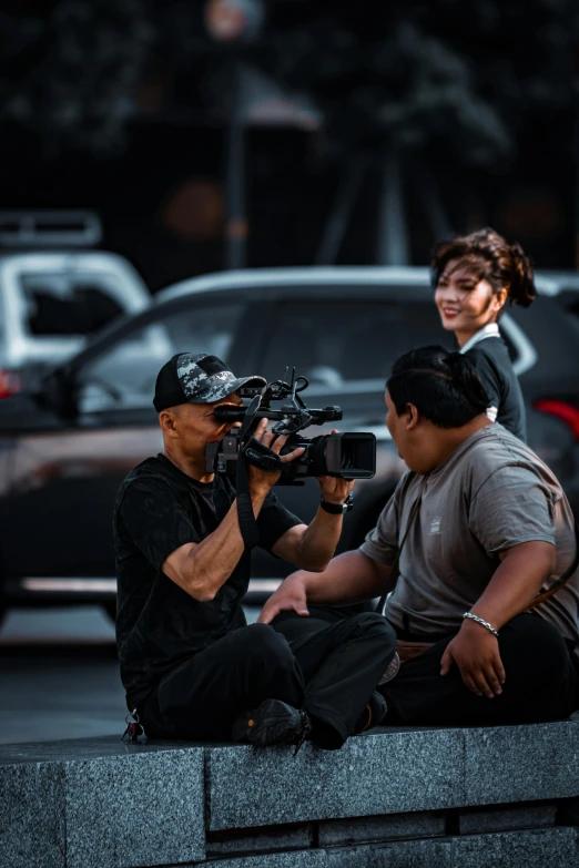 a man and a woman sit on the ledge near cars and take pos