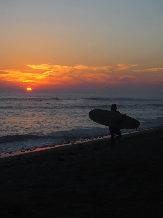 a man holding his surfboard as the sun sets