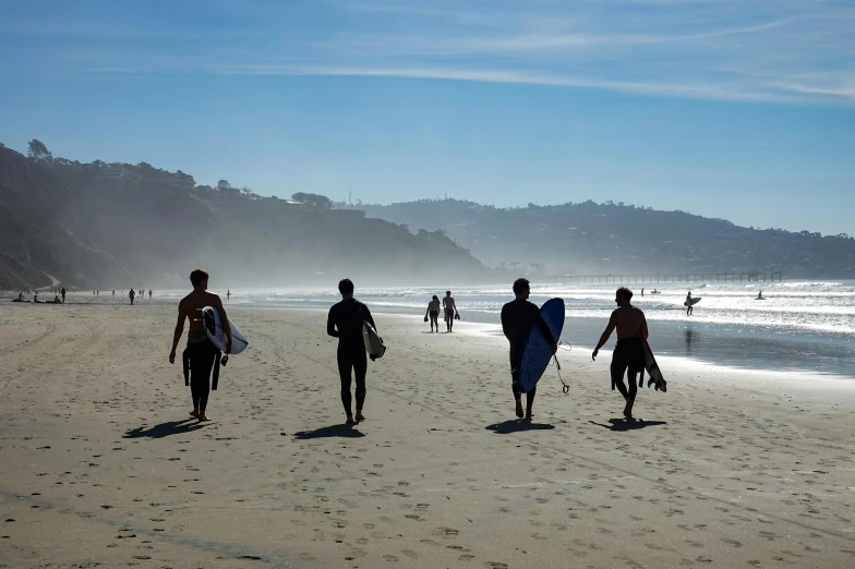 three people with surfboards walking on the beach