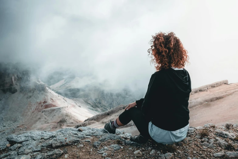 a woman sits on top of the mountain, looking at the valley