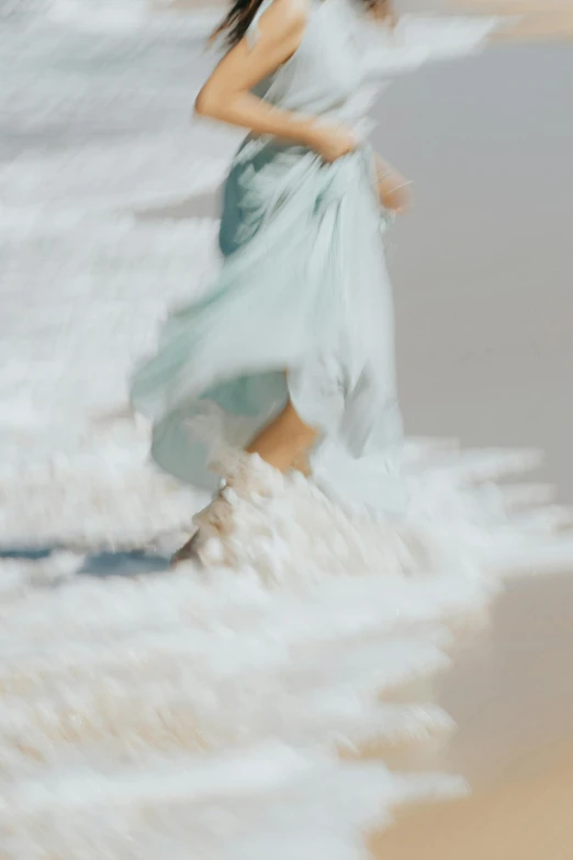 a woman in a light blue dress walking on the beach