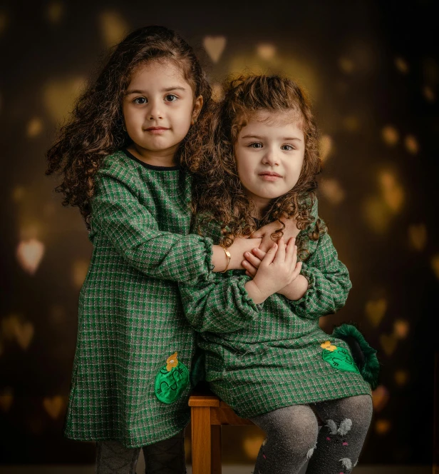 two small children, one is sitting on a chair and the other has her hands crossed