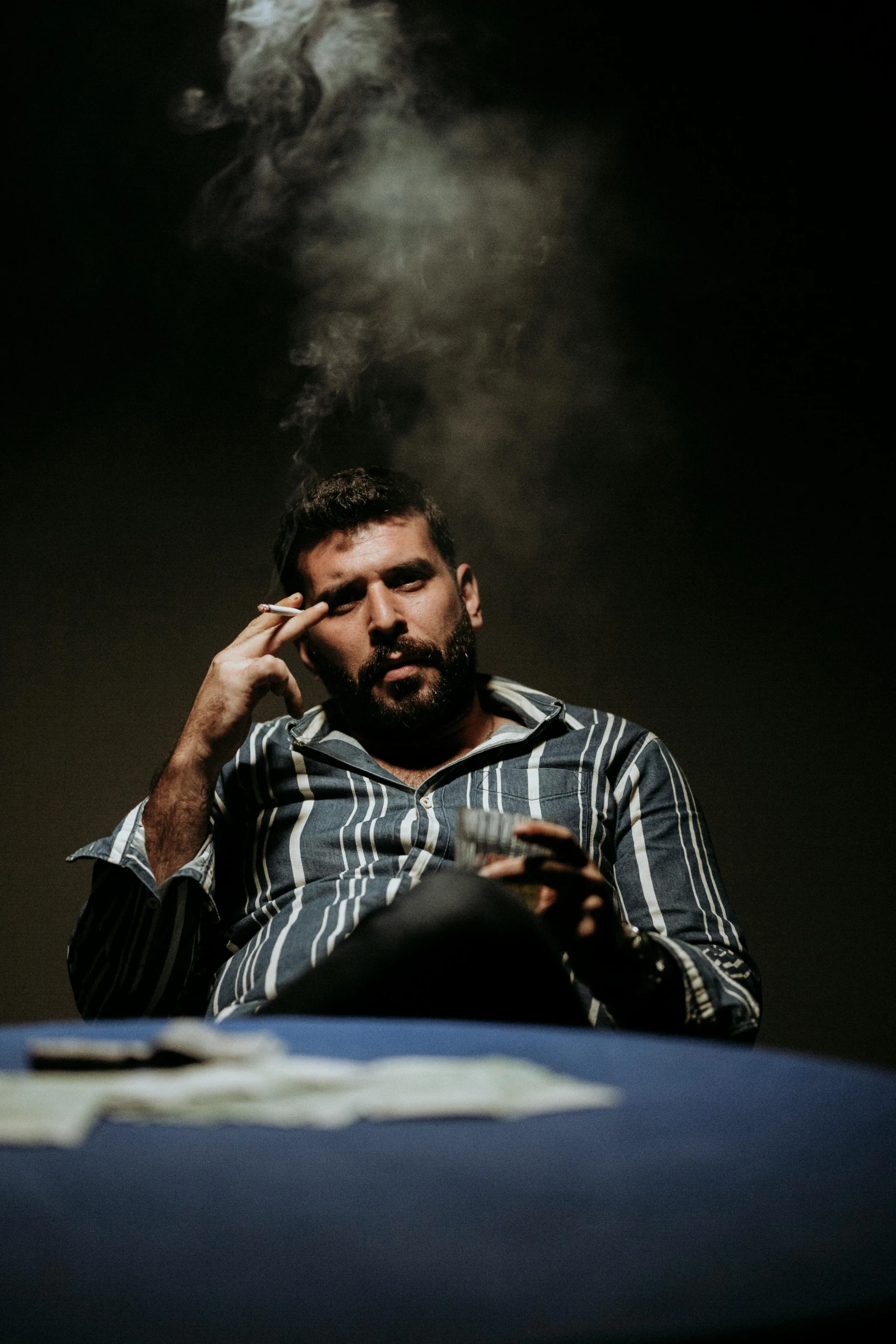 man smoking cigarette and reading newspaper while looking at his cell phone