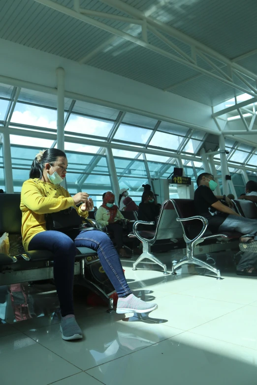 two women sitting on a bench in an airport with people watching