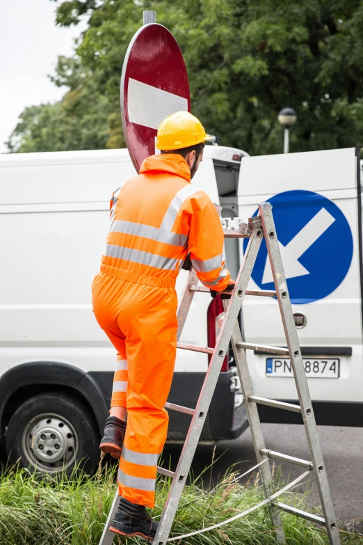 a man in orange overalls and a yellow helmet climbing on a ladder