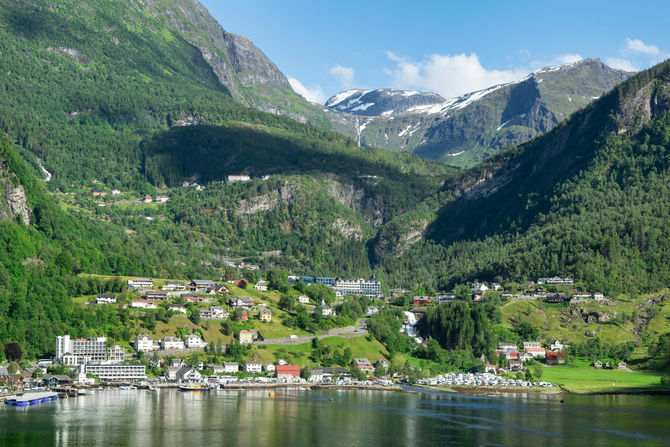 the green mountains are behind the village and river