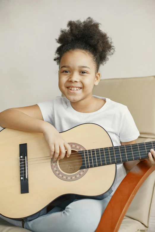 a child sitting on a chair and holding an acoustic guitar