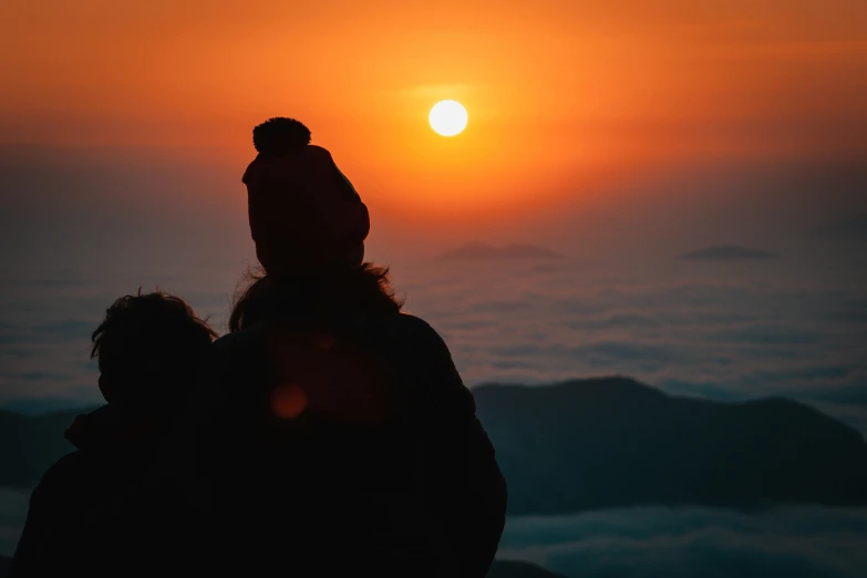 a couple sitting on top of a mountain watching the sun rise