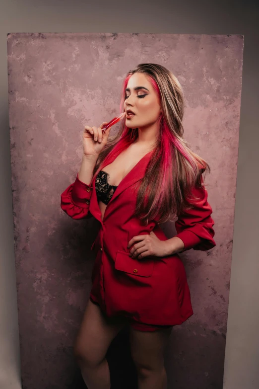 a woman wearing red is smoking and standing near a wall