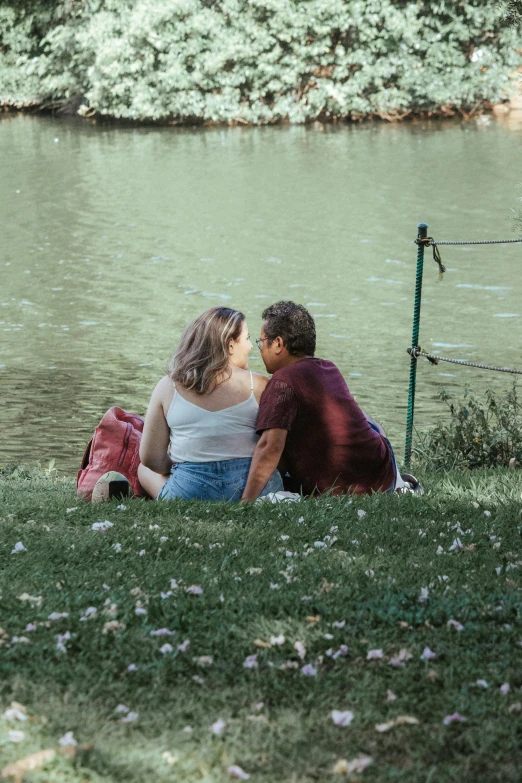 a young man and a young lady are sitting by a lake