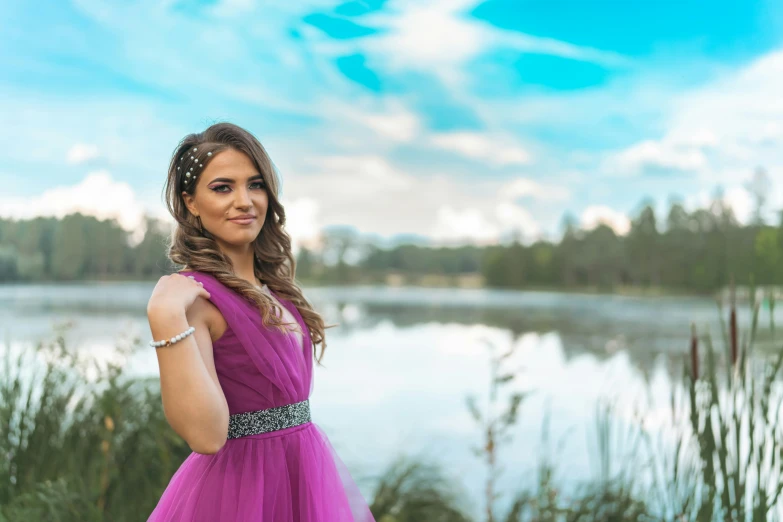 a woman in a purple dress standing on the shore of a lake