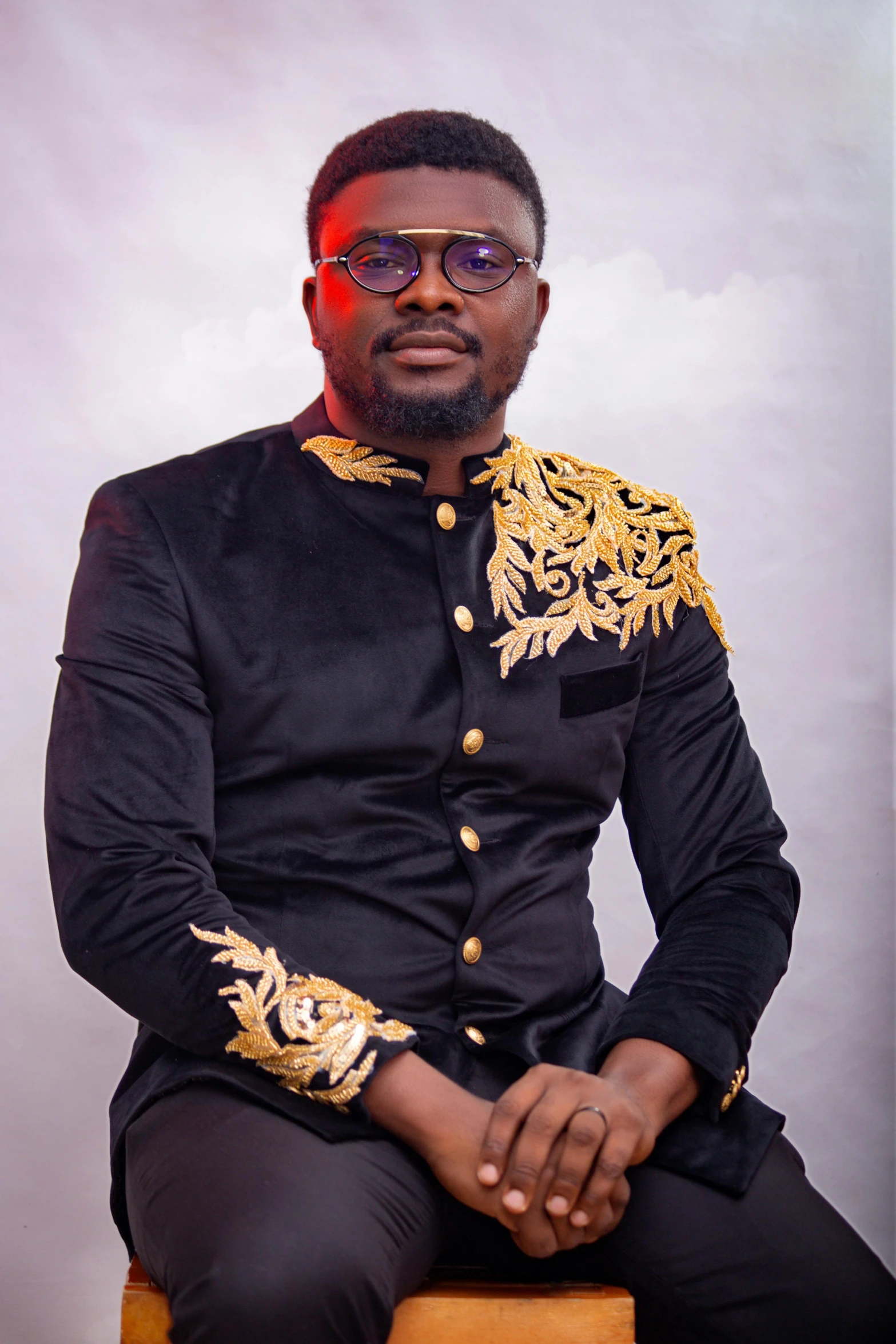 a man sitting down wearing a black and gold suit