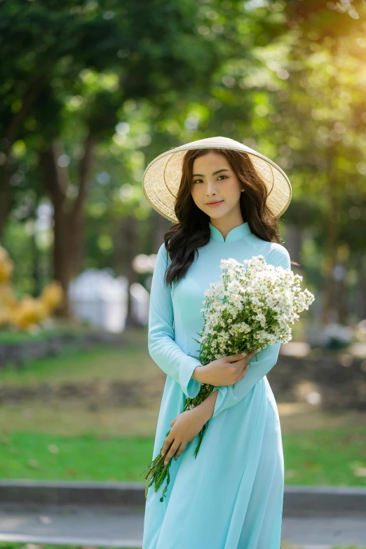 an asian lady in a blue dress and straw hat with a bouquet of flowers