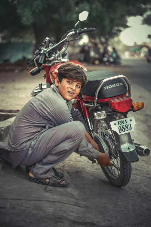 a young man in a dark - colored suit crouching by a motorcycle