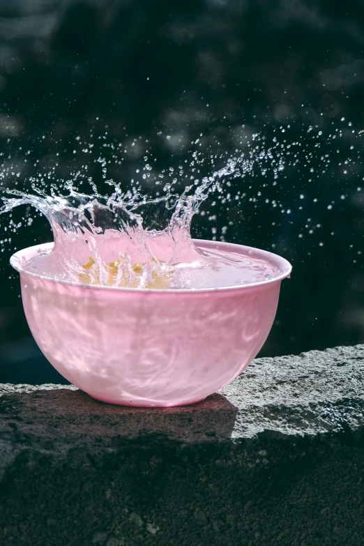 a pink bowl filled with water floating on top of a cement slab