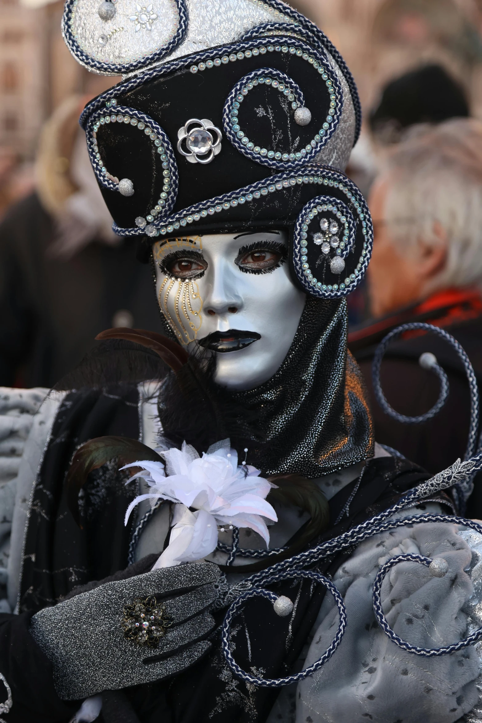 a man with dark hair and white face paint, wearing a hat that has round faces