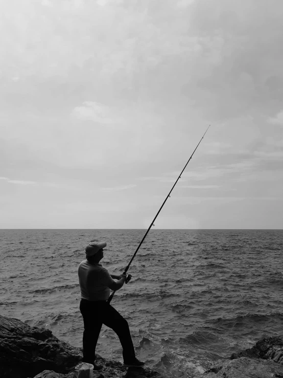 a man holding a fishing rod on top of a rock