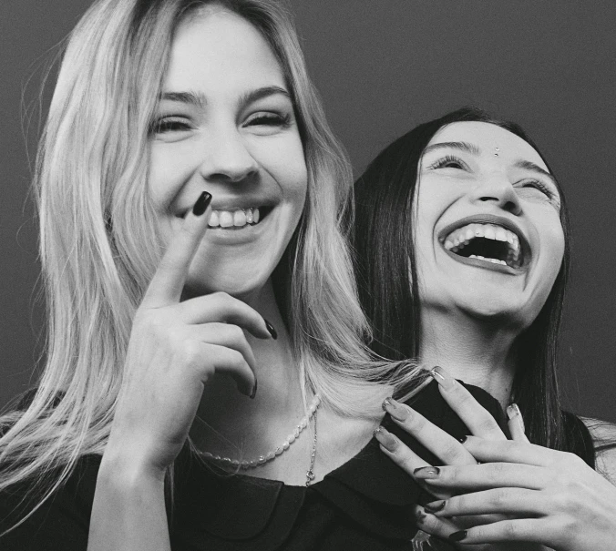 two girls are laughing while one looks at her phone